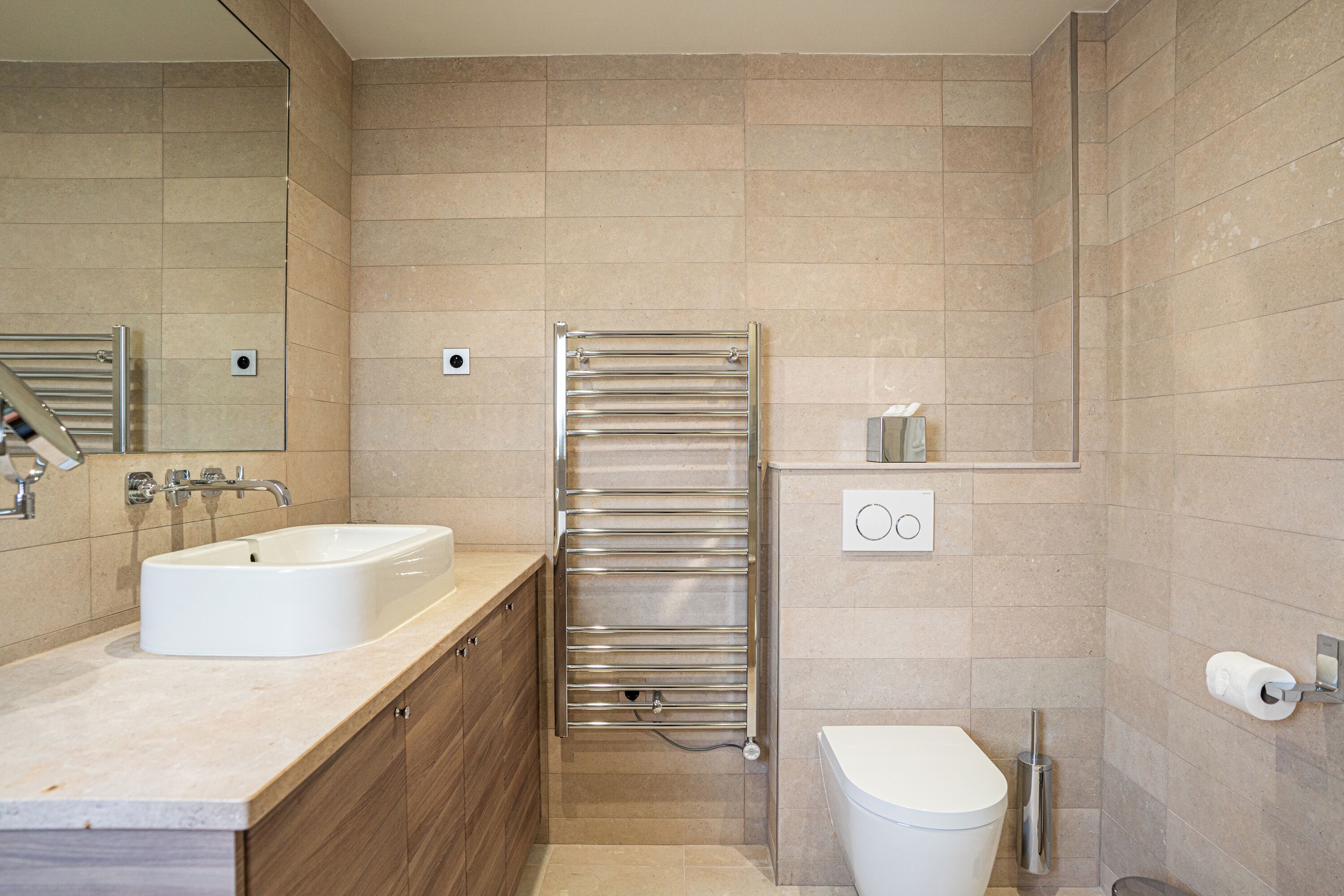 A modern bathroom with a sink, mirror, towel rack, toilet, and a small shelf with toiletries.