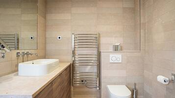 A modern bathroom with a sink, mirror, towel rack, toilet, and a small shelf with toiletries.