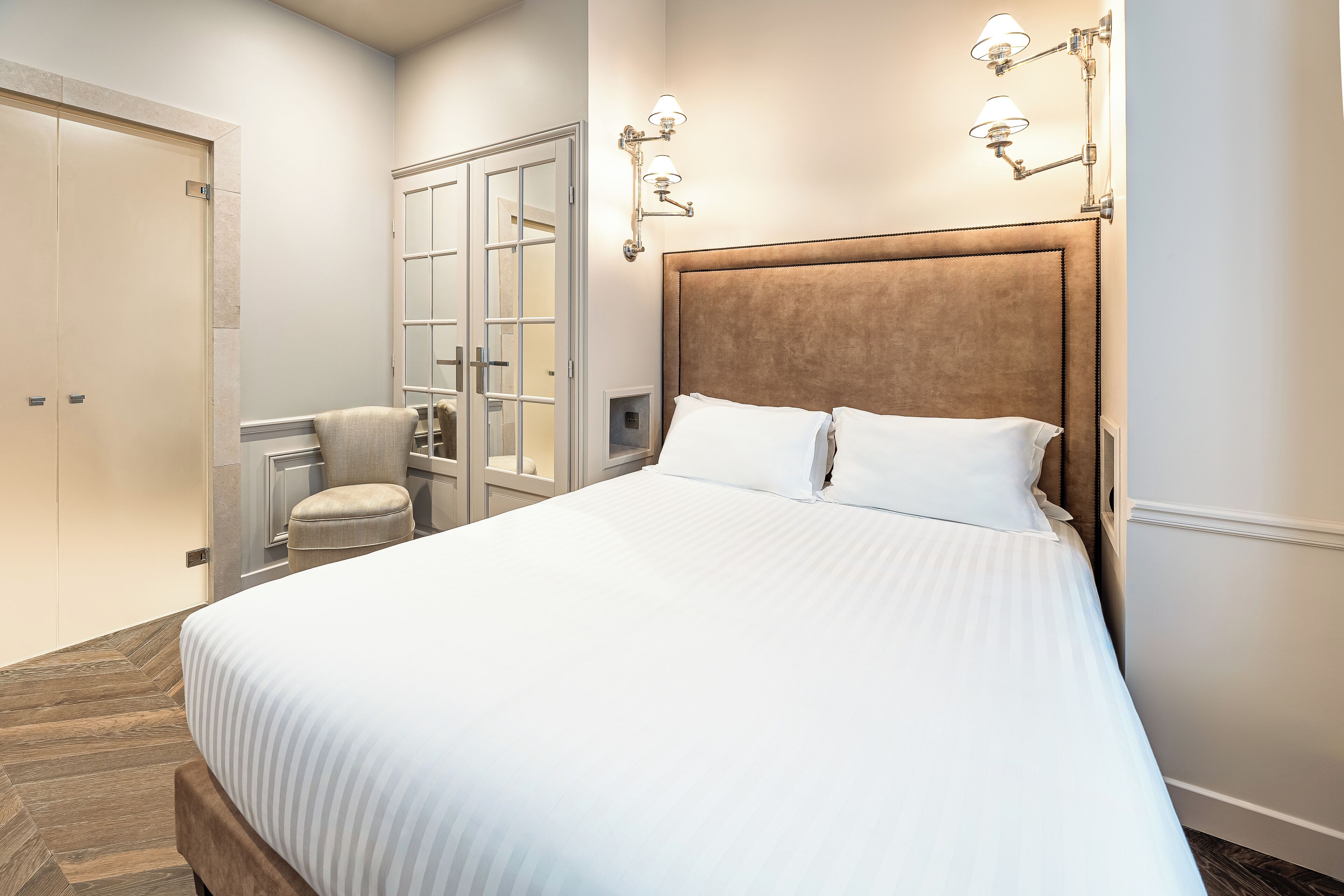 A bedroom with a large bed, a wardrobe, a seating area, and a glass door closet.