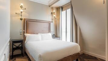 Una cama bien hecha con sábanas blancas, un cabecero de madera y dos mesitas de noche con lámparas.