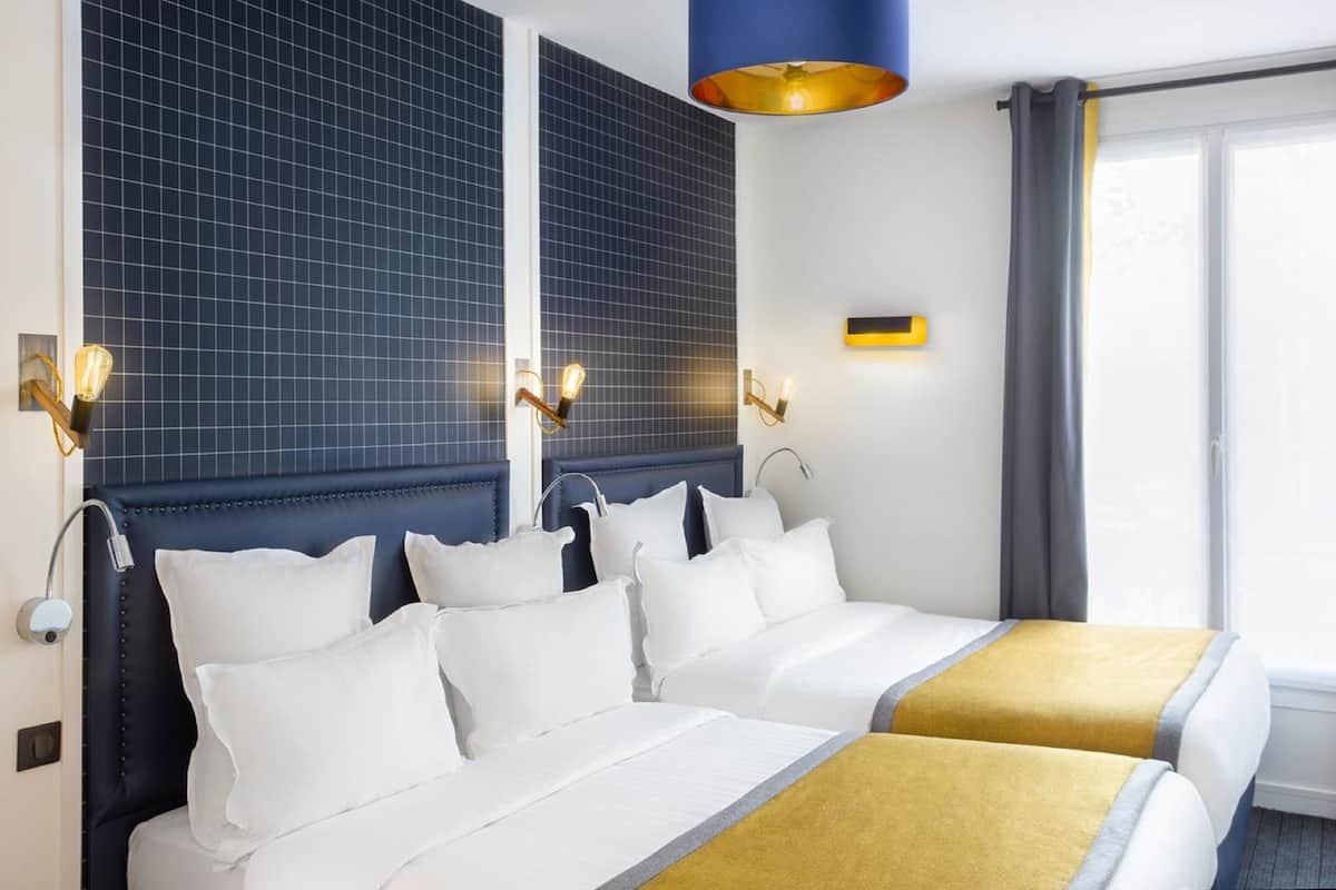 A hotel room with two beds, a large window with curtains, and a blue accent wall.