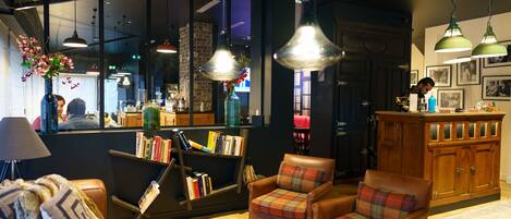 A cozy lobby with leather armchairs, a bookshelf, and pendant lighting.