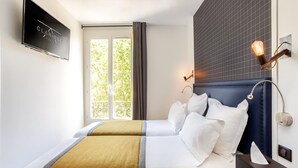 A hotel room with a bed, a TV mounted on the wall, and a window with curtains. - Hôtel Clarisse (Paris)