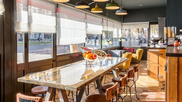 A modern dining area with a glass table, colorful pendant lights, and a view of the street outside. - Hôtel Clarisse (Paris)