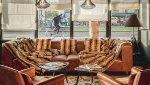 A cozy living area with a fur-covered sofa, leather armchairs, and a coffee table. Large windows offer a view of the street outside. - Hôtel Clarisse (Paris)