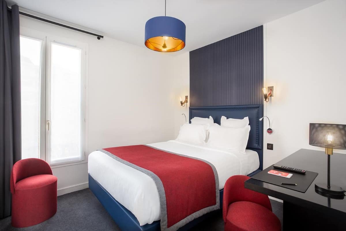 A hotel room with a bed, a desk, a chair, and a window.