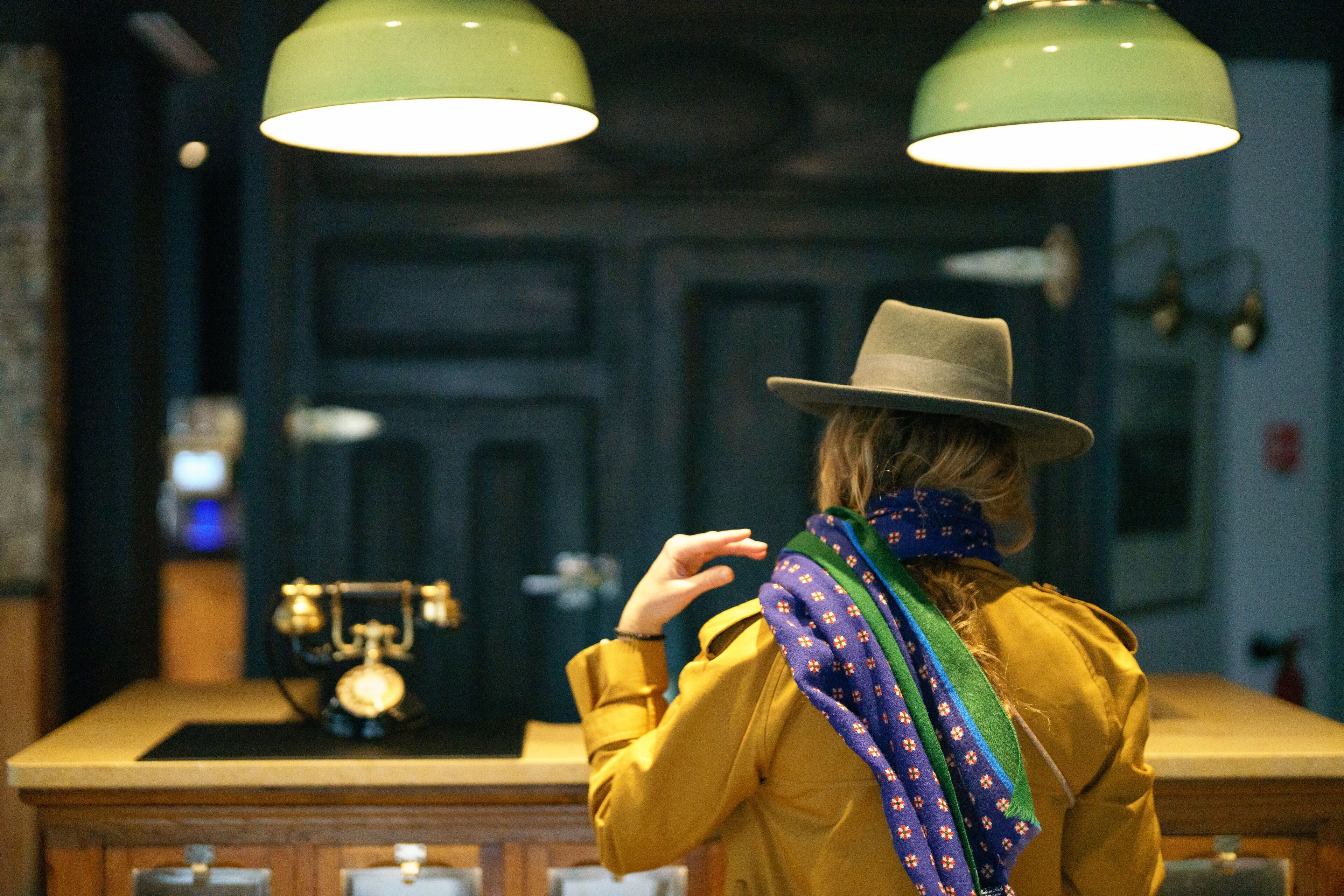 A person in a yellow jacket and hat standing in a room with a wooden counter and two green pendant lights.