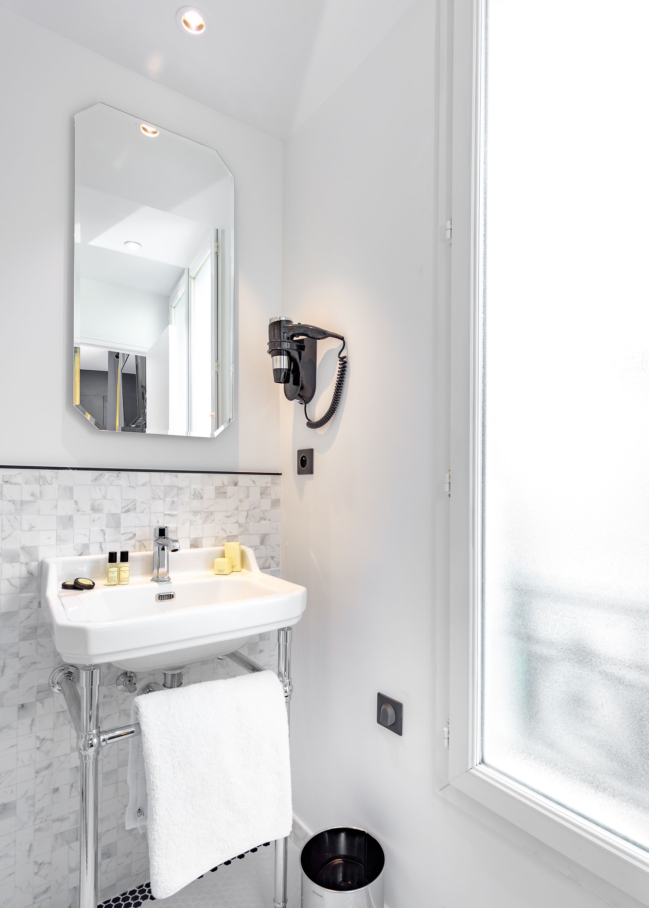 Un baño moderno con un lavabo blanco, espejo y secador de pelo montado en la pared.