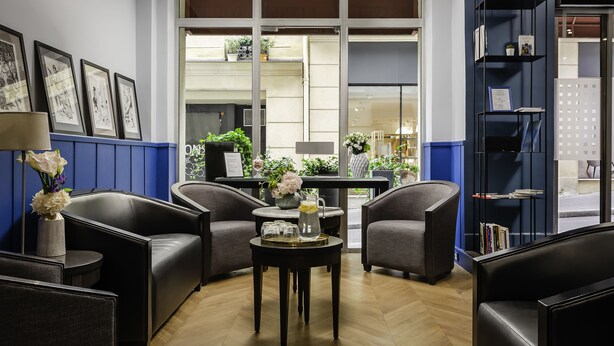 A modern lobby with leather seating, a coffee table with a tray, framed artwork on the wall, and a bookshelf. - Hôtel Elysée Etoile (Paris)