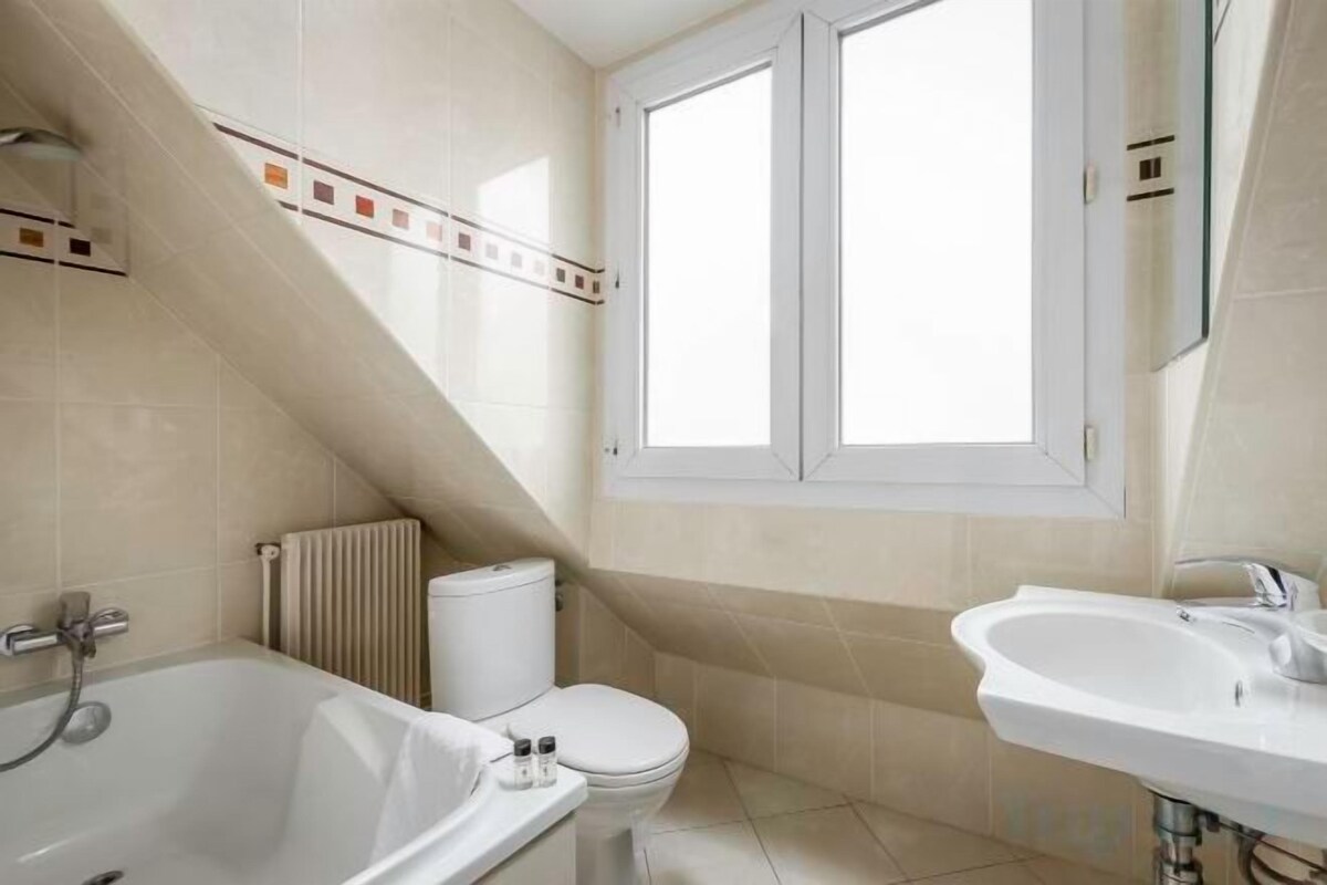 A bathroom with a bathtub, toilet, and sink, featuring a window and tiled walls.