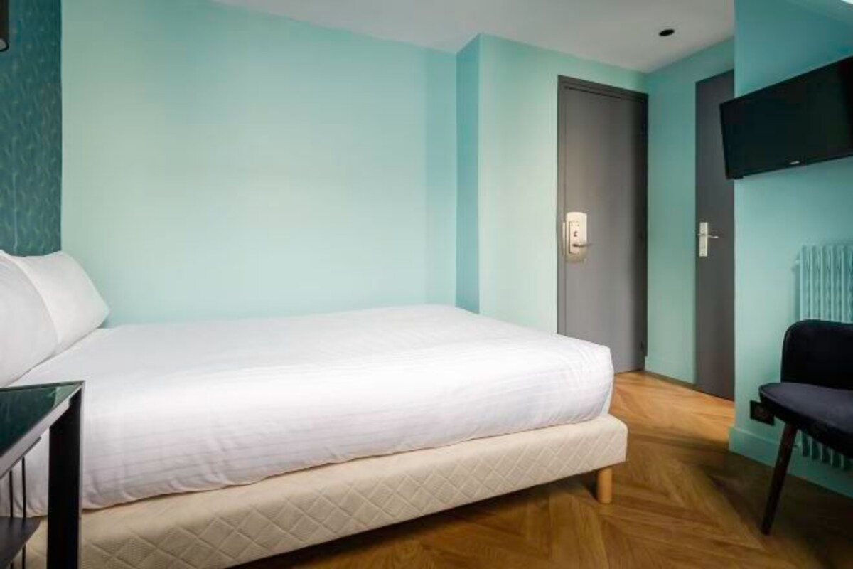 A bedroom with a bed, a chair, a TV mounted on the wall, and a door.