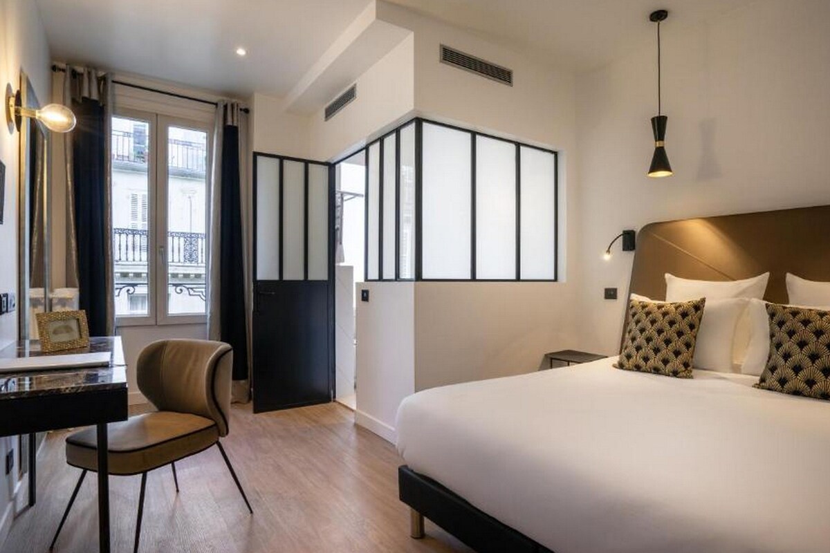 A modern hotel room with a large bed, a desk, and a chair.