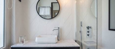 Un baño moderno con lavamanos blanco, encimera negra y un espejo redondo.