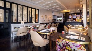 A restaurant with round tables and chairs, a bar area, and a modern ceiling design. - Hotel Royal Opera (Paris)