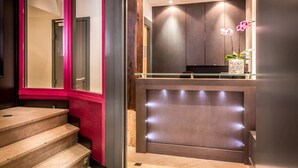 A modern reception area with a glass partition, a reception desk, and a decorative orchid plant. - Hotel Royal Opera (Paris)
