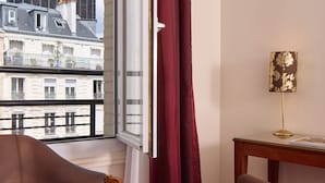 A hotel room with a view of a tall building, a table with a magazine, and two chairs. - Timhotel Tour Montparnasse (Paris)