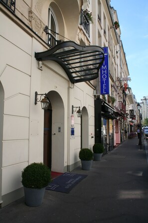 A hotel facade with a prominent 'HOTEL' sign, arched doorways, and potted plants. - Timhotel Tour Montparnasse (Paris)