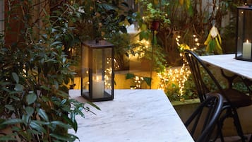 Un espace de restauration en plein air, avec une table et des chaises, entouré de verdure et illuminé de guirlandes lumineuses.