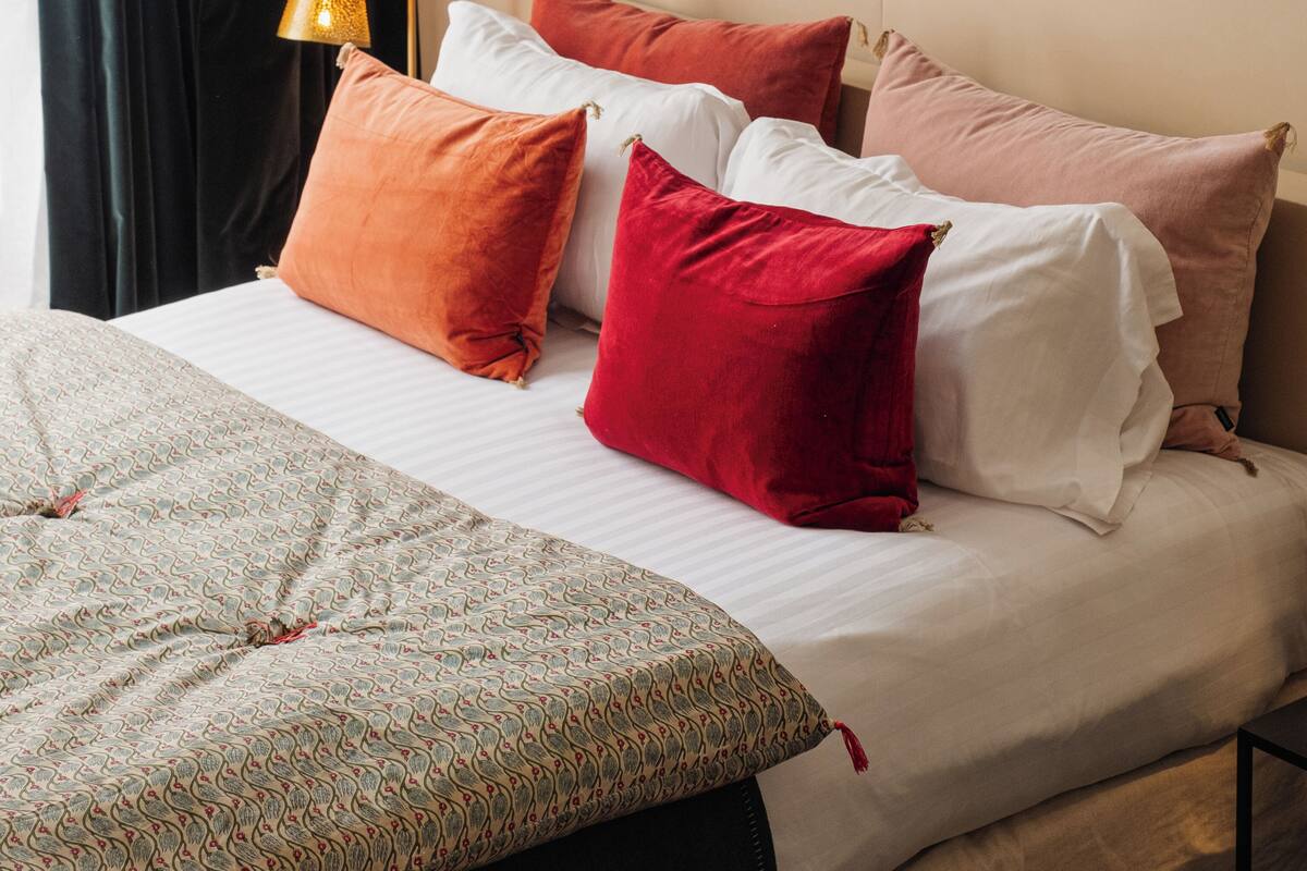Una cama bien hecha con ropa de cama estampada, una variedad de almohadas y una lámpara de noche.