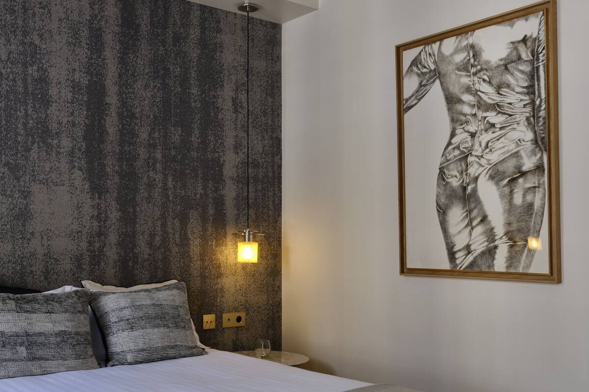 Un dormitorio moderno con una pared texturizada, una obra de arte enmarcada, una cama con almohadas y una mesita de noche con una lámpara.