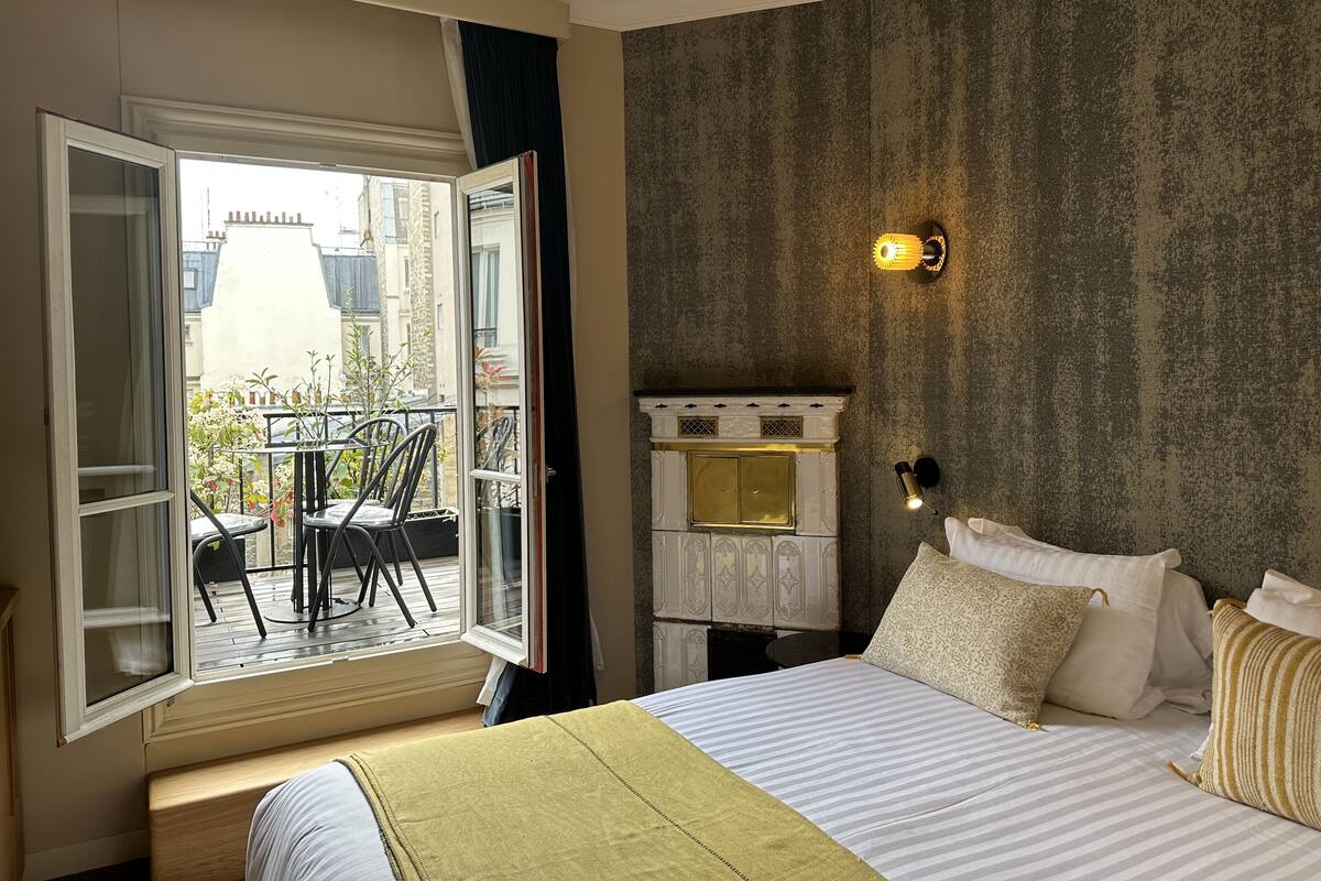 Una habitación de hotel con una cama grande, un balcón con sillas y vistas a edificios.