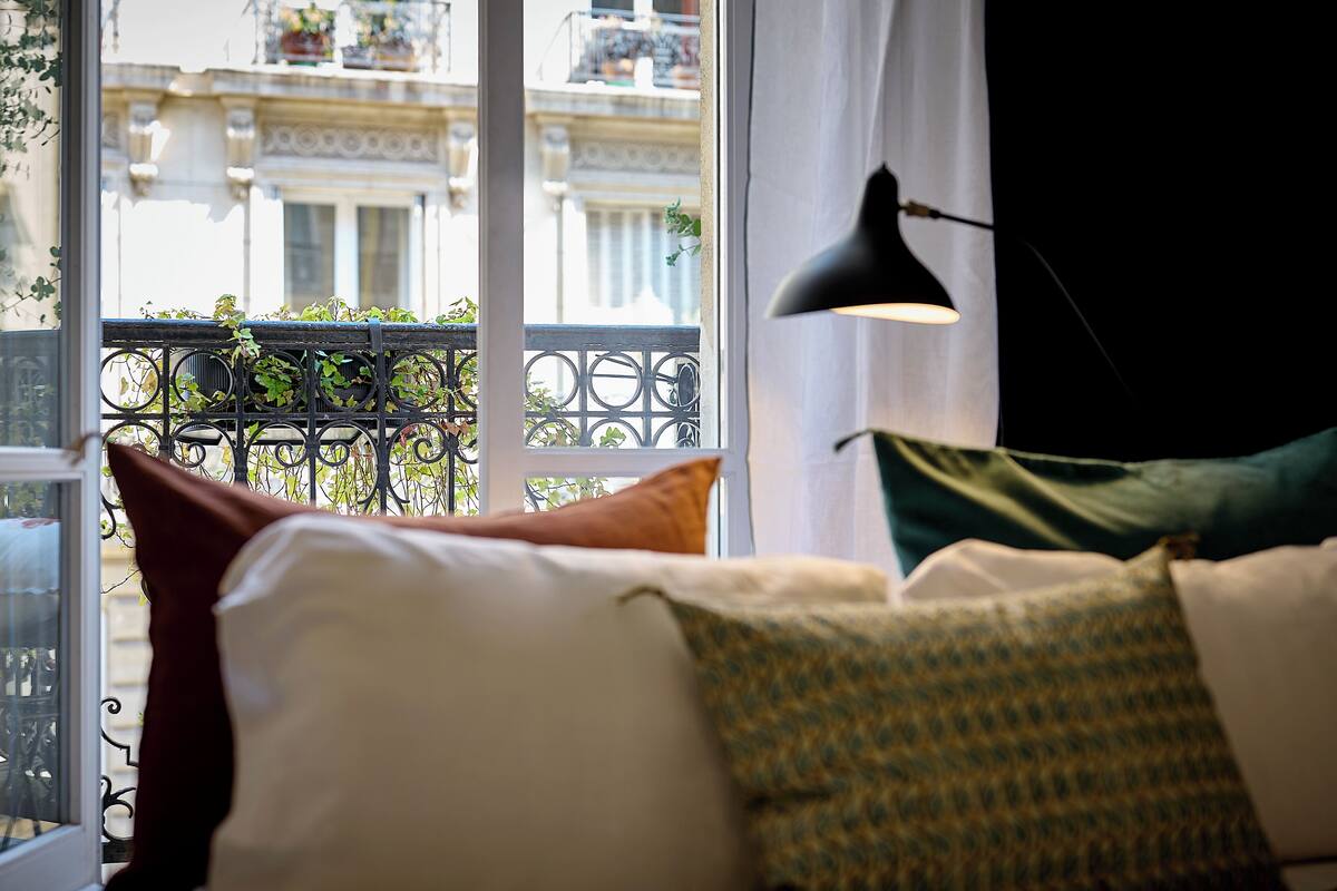 Una habitación con una cama, un ventanal con vista a un edificio y una lámpara de pie de color negro.