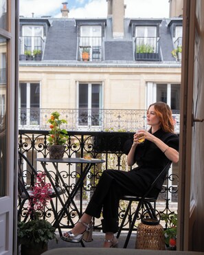 A woman sitting on a balcony with a view of buildings and potted plants. - Hôtel Beauséjour Ranelagh (Paris)