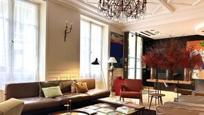 Amplia sala de estar con un sofá de cuero marrón, una mesa de centro redonda con libros, un sillón rojo y un candelabro.
