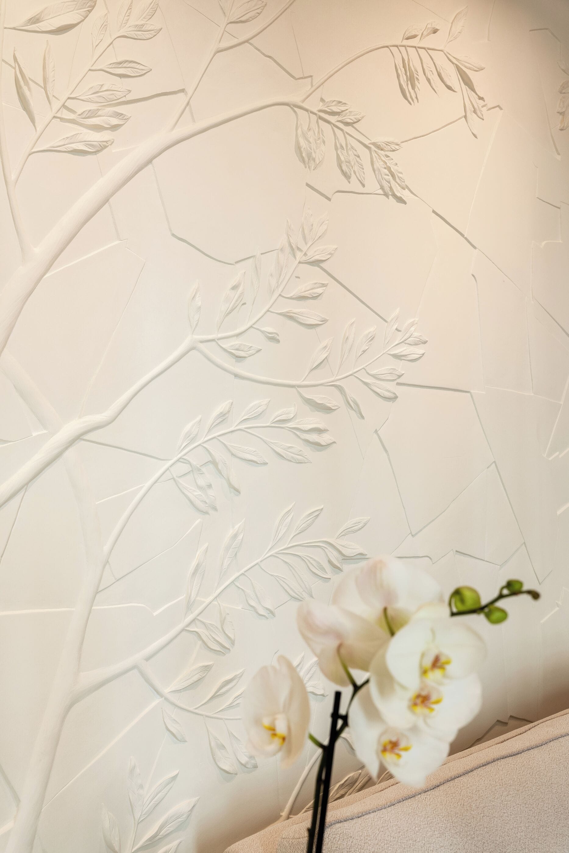 A wall with a floral pattern and a vase with white orchids.