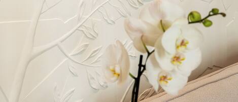 A wall with a floral pattern and a vase with white orchids.