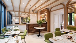 A dining area with green upholstered chairs, white tables, and a central round table with a vase of flowers. - Villa Madame (Paris)
