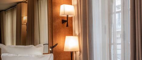 Habitación de hotel con una cama grande, dos lámparas de noche, un cabecero de madera y vistas a la Torre Eiffel a través de cortinas translúcidas.