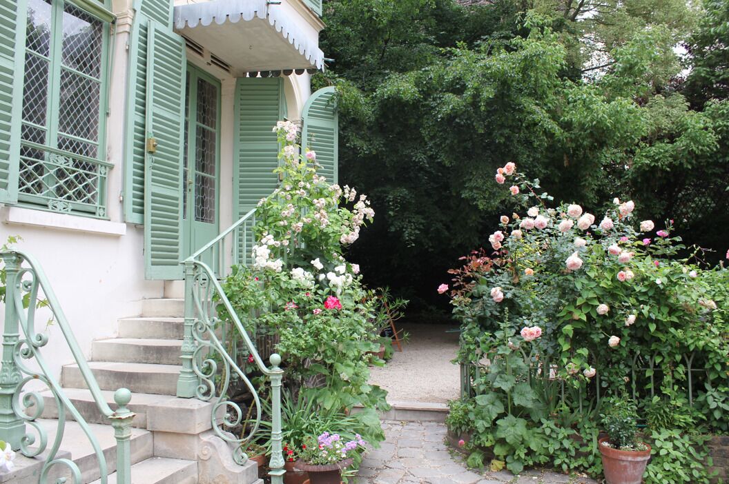 A garden with a stone staircase leading to a house with green shutters and a white awning. - Hôtel Sacha (Paris)