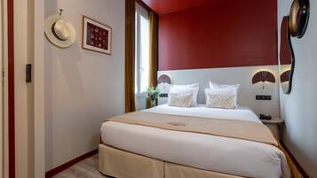 Une chambre d’hôtel avec un grand lit, une table de chevet, un ventilateur fixé au mur et une fenêtre avec des rideaux.