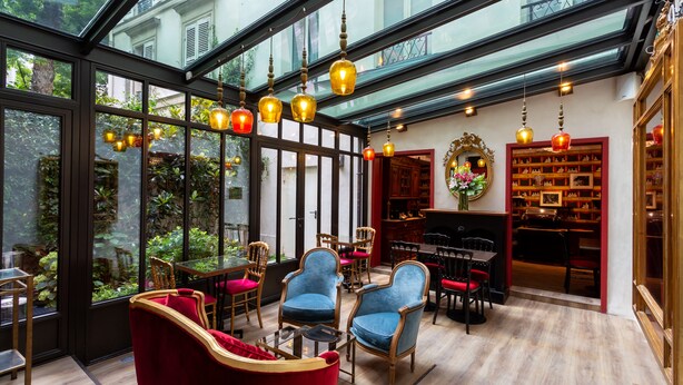 A spacious room with a glass ceiling, wooden flooring, and a variety of seating including red velvet sofas and blue armchairs. - Hôtel Sacha (Paris)