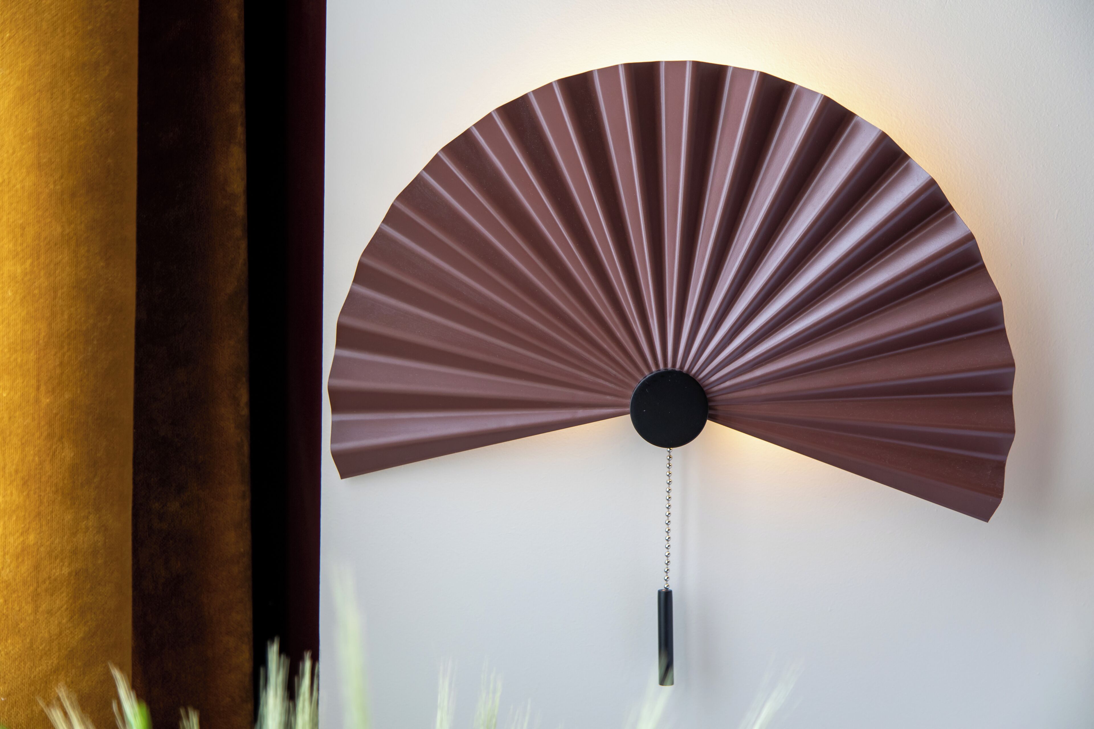 Un ventilador de pared con diseño radial, un núcleo central negro y una cadena colgante.