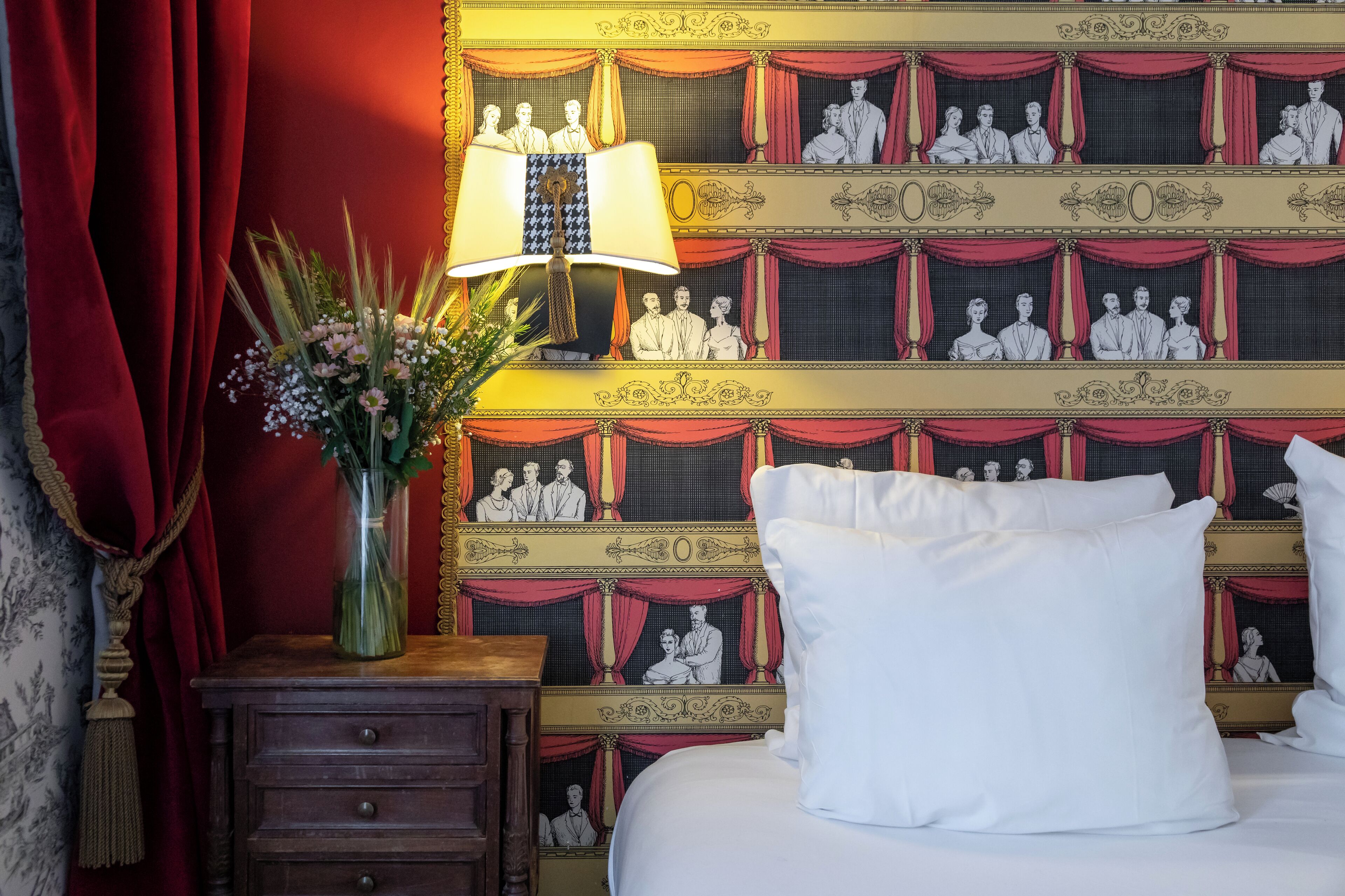 A hotel room with a bed, a nightstand with a lamp, and a wall with a patterned design.