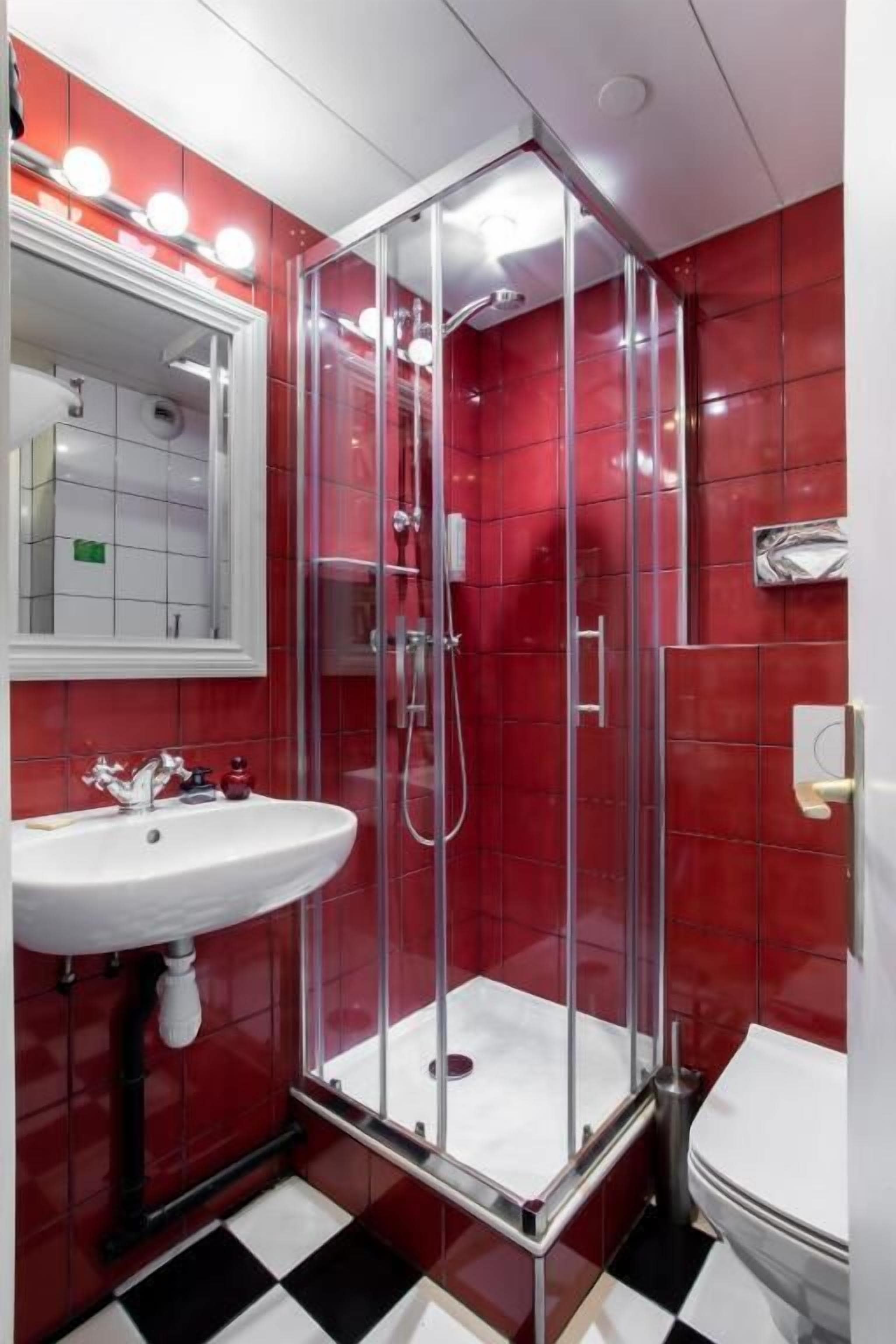A bathroom with a glass-enclosed shower, a white sink, and a red-tiled wall.
