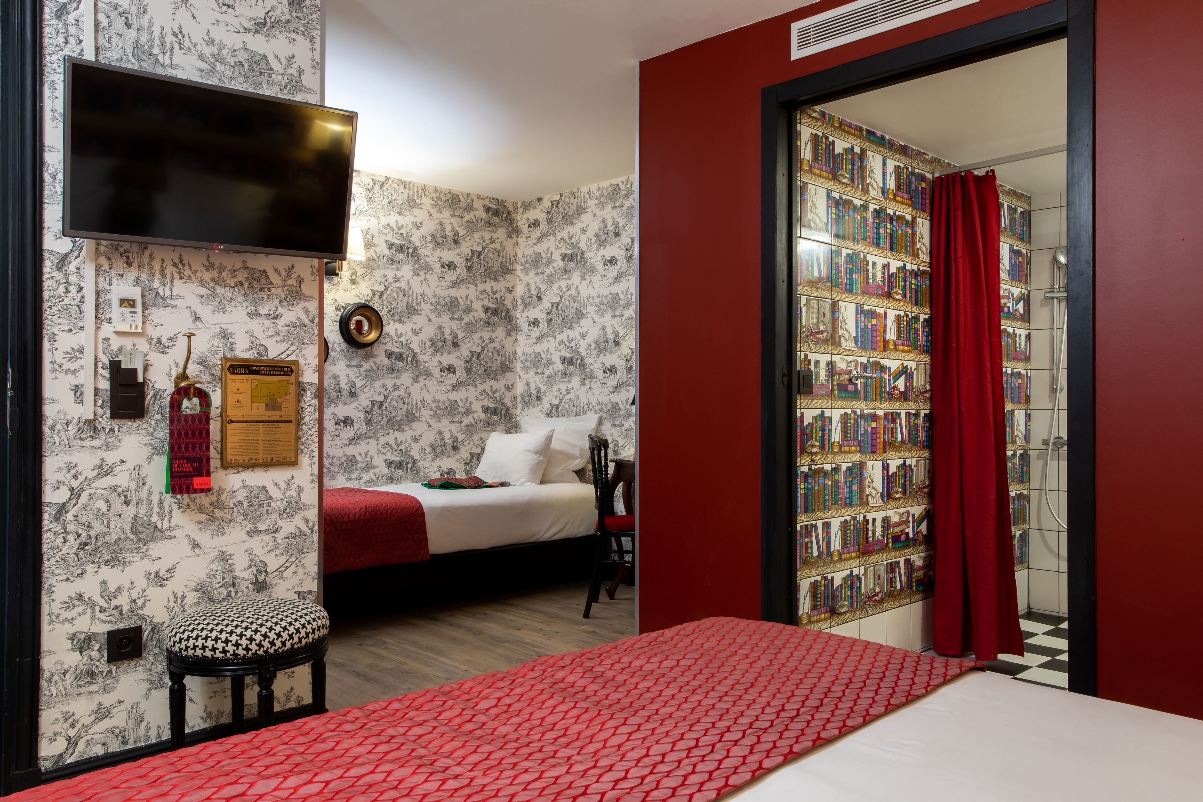 Un dormitorio con una cama, un taburete pequeño, una estantería y un televisor.