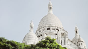 Un edificio grande de color blanco con cúpula principal y varias cúpulas más pequeñas, y una estatua en primer plano.