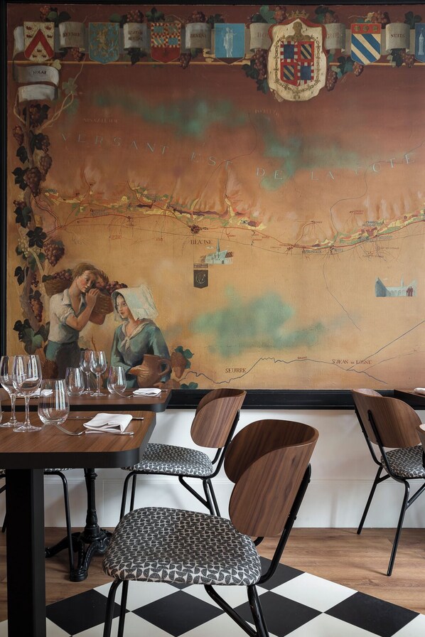 Interior de restaurante con un mural grande de un mapa, sillas de madera y copas de vino sobre la mesa.