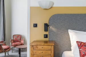 Una habitación de hotel con cama, mesita de noche de madera, una silla, una lámpara de pared y una pared con textura.
