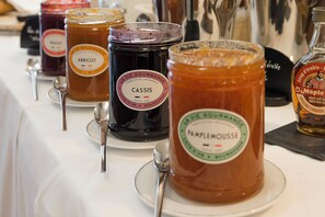 A table with jars of food items, each labeled with the name of the food and the brand. - Hôtel de la Poste (Beaune)