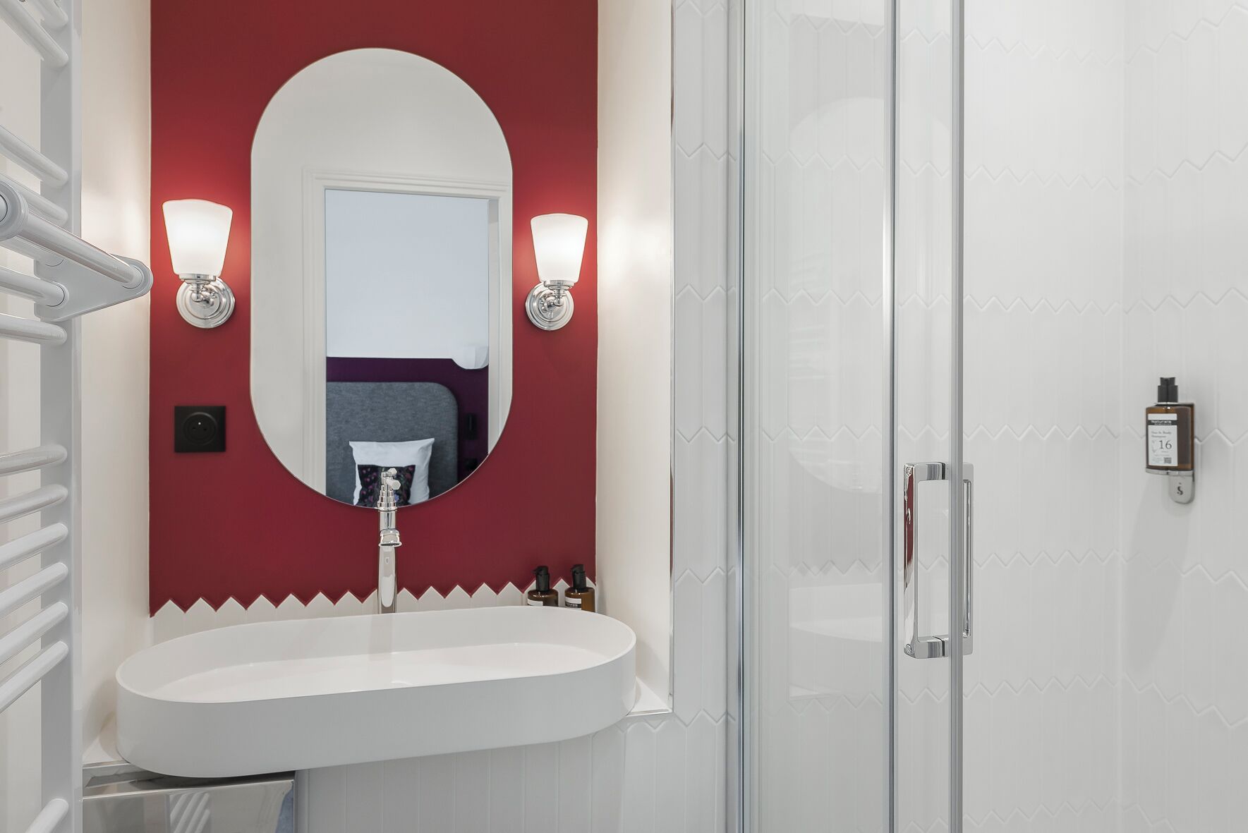 Un baño con lavamanos blanco, un espejo ovalado grande y dos luces en la pared.