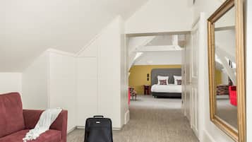 Een slaapkamer met een bed, een rode bank, een zwarte koffer en een grote spiegel.