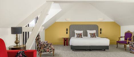 A bedroom with a bed, a red chair, a small table, and a lamp.