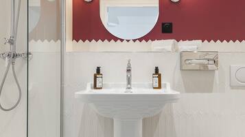 Casa de banho com lavatório pedestal branco, cabine de duche em vidro e parede com destaque em vermelho.
