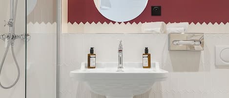 A bathroom with a white pedestal sink, a glass shower enclosure, and a red accent wall.