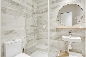 A modern bathroom with a glass-enclosed shower, a white toilet, and a round mirror above a sink.