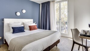 A hotel room with a large bed, a desk with a chair, and a view of the outdoors through a window. - Hotel Courseine (Courbevoie)